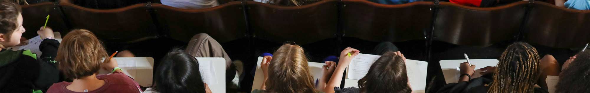 A generic picture showing students sitting in a row with notebooks.